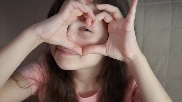 Showing symbol of love by teen face. A teen girl with happy feelings show the finger heart by her face indoor.