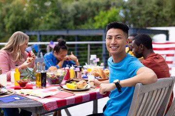 Portrait of happy diverse group of friends talking and having dinner at balcony with flags of usa