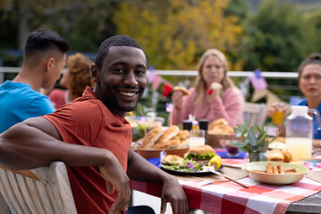 Portrait of happy diverse group of friends talking and having dinner at balcony with flags of usa