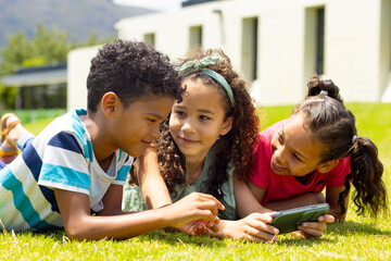 Biracial boy and girls are lying on the grass, looking at a smartphone together