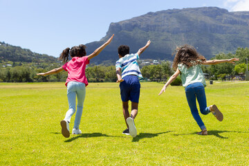 Three biracial children run across grassy field, full of joy
