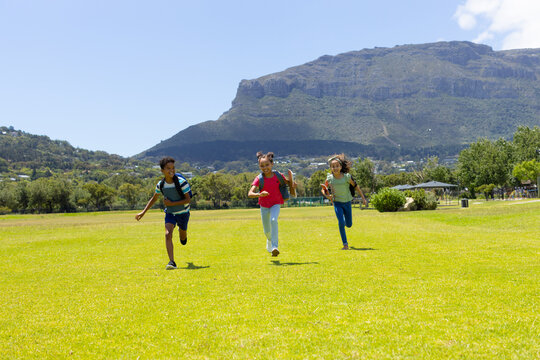 Three biracial children run across grassy field, mountains behind