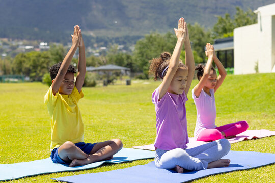 Biracial children practice yoga outdoors, sitting on colorful mats