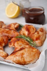 Raw marinated chicken wings and rosemary on light table, closeup