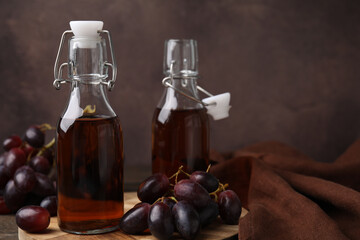 Bottles with wine vinegar and grapes on wooden table, closeup