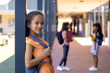 Biracial girl with a backpack smiles, standing in a school corridor with copy space