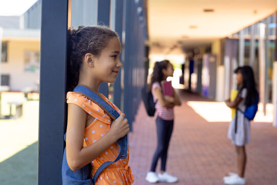 Biracial girl with a polka dot dress stands by a pillar at school, smiling, with copy space