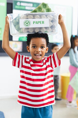 In school, young African American boy holding up paper recycling bin in classroom