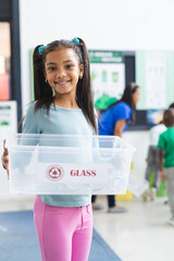 In school, young African American girl proudly holds recycling bin in classroom