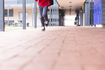 In school, young biracial male student is running along a corridor outdoors with copy space