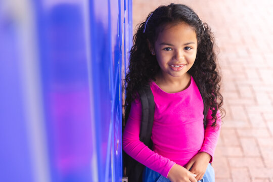 In school, outdoors, young biracial girl leaning against a locker, wearing a pink top