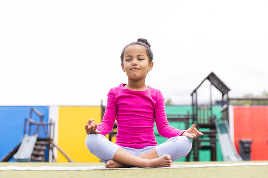 In school, young biracial girl sitting cross-legged outdoors, practicing yoga
