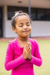 In school, young biracial girl with closed eyes is standing outside doing yoga