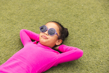 In school, biracial young girl wearing sunglasses is lying on grass outdoors