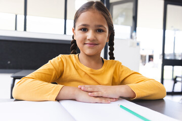 In school, biracial young girl sitting at a desk in a classroom, smiling at camera