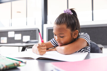 In school, in the classroom, young biracial girl focusing on writing in her notebook
