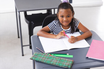 In school, young biracial girl sitting at a desk writing in classroom