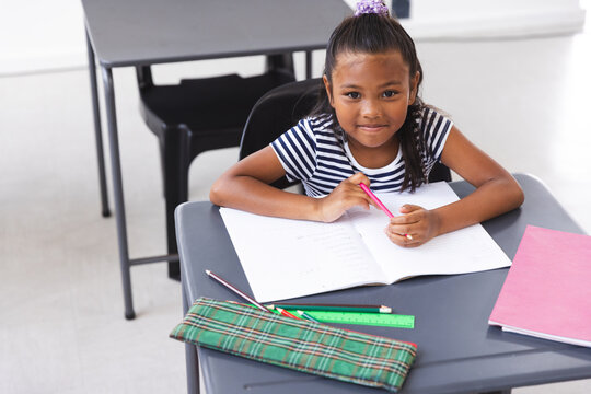 In school, young biracial girl sitting at a desk writing in classroom - Powered by Adobe