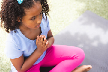 Biracial girl practices yoga outdoors at school, with copy space - Powered by Adobe