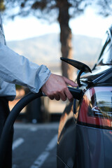 Hand charging EV plug to electric vehicle with natural background for traveling by electric car concept.