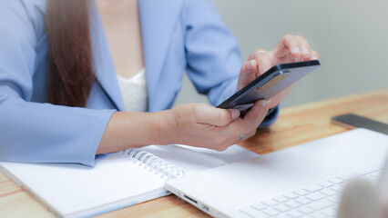 Fototapeta premium A woman in a blue suit is using her cell phone while sitting at a desk. Concept of productivity and focus, as the woman is likely working on a task or communicating with someone