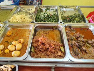 Food stalls share a variety of buffet menus with vegetables, chicken curry sauce, beef, eggs, tofu, tempeh. the waiter prepares the food. Menu in glass display case. Asia and asian food. Pile.