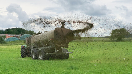A farm tractor sprays its manure from the tanker onto a field. Manure is used as fertilizer in...