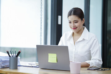 Sharing good business news. Attractive young businesswoman talking on the mobile phone and smiling while sitting at her working place in office and looking at laptop PC.