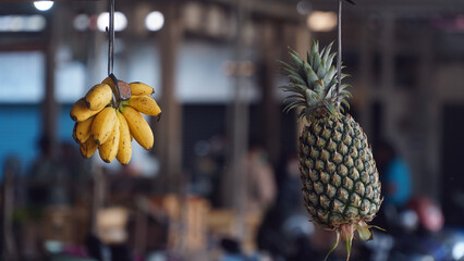 Bananas and pineapples are hung with ropes. Focus selected. Blurred background