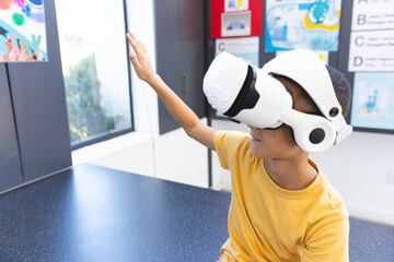In a school, a biracial boy explores virtual reality using a headset in the classroom