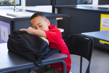 Biracial boy rests his head on a backpack at school