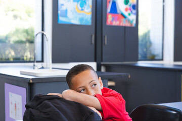 Biracial boy rests his head on his arms at school