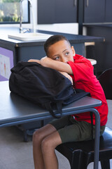 Biracial boy sits at a school desk, looking thoughtful