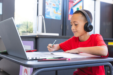 Biracial boy studies intently in a school classroom using a laptop, with copy space