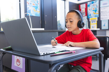 Biracial boy studies intently in a school classroom using a laptop, with copy space