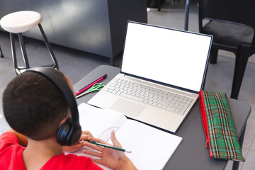 Biracial boy studies at a school desk using a laptop, with copy space