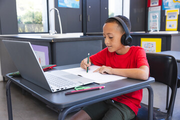 Biracial boy studies intently in a school classroom using a laptop, with copy space