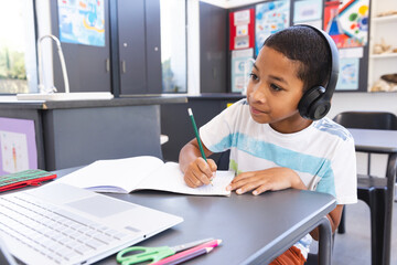 Biracial boy studies intently at school using a laptop