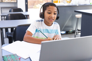 Biracial boy studies in a school classroom using a laptop - Powered by Adobe