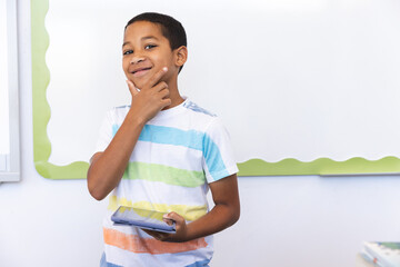 Biracial boy holds a tablet in a classroom setting in school