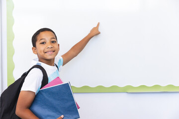 Biracial boy points at a whiteboard in a classroom at school