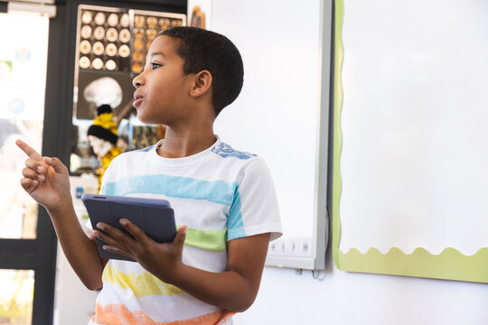 Biracial boy using a tablet in a classroom at school, with copy space