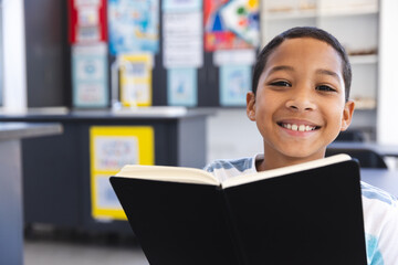 Biracial boy enjoys reading a book in the classroom at school