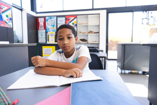Biracial boy sits at a school desk in a classroom, with copy space, at school