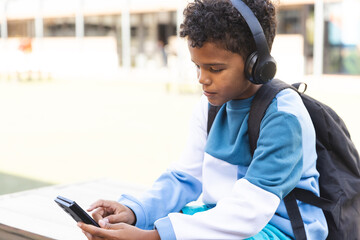 Biracial boy enjoys music on his phone outdoors at school, with copy space