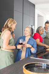 Diverse senior female friends holding wine glasses, smiling at home