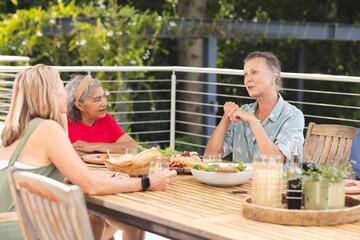 Diverse senior female friends wearing casual clothes, chatting over meal outdoors