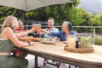 Diverse senior female friends enjoying meal outdoors, toasting glasses