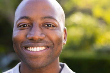 Outdoors, young African American man smiling warmly with lush greenery background