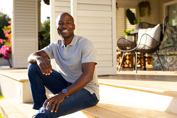 Outdoors, African American young man sitting on porch steps, smiling at camera